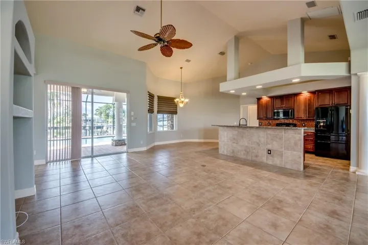 Kitchen with tasteful backsplash, light tile patterned floors, ceiling fan with notable chandelier, high vaulted ceiling, and black refrigerator with ice dispenser