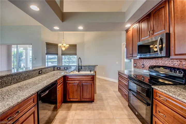 Kitchen featuring tasteful backsplash, black appliances, sink, light tile patterned floors, and light stone countertops