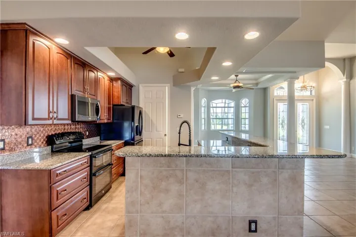 Kitchen featuring black appliances, ceiling fan, tasteful backsplash, light stone countertops, and ornate columns