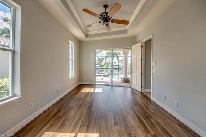 Unfurnished room featuring hardwood / wood-style floors, a healthy amount of sunlight, ceiling fan, and a raised ceiling