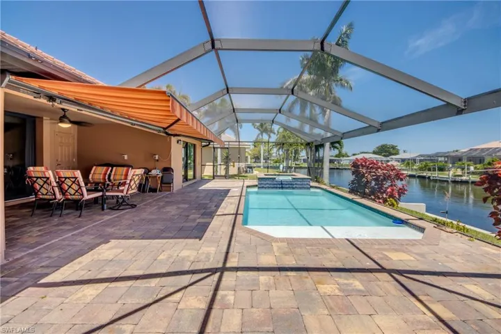 View of swimming pool featuring a water view, a pool with connected hot tub, a sunroom, glass enclosure, and a patio area