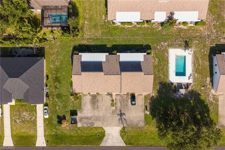 Aerial perspective showcasing a residential lot with a paved driveway, mature trees, and visible rooftops