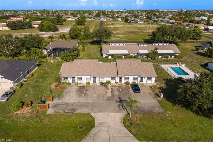 Duplex property featuring a paved parking area and mature landscaping