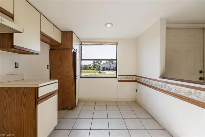 Kitchen space featuring tile flooring, a large window, recessed lighting, and upper and lower cabinetry with wood-finish bases and light-colored doors