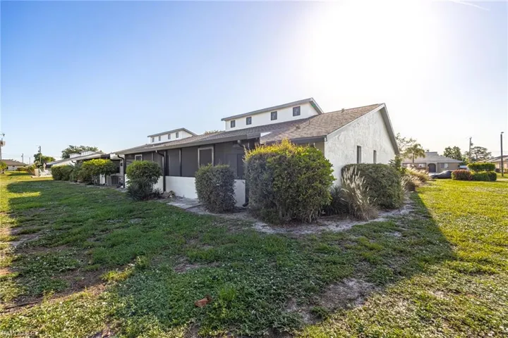 Stucco exterior with multiple screened patio areas, multiple air conditioning units, and mature shrubbery