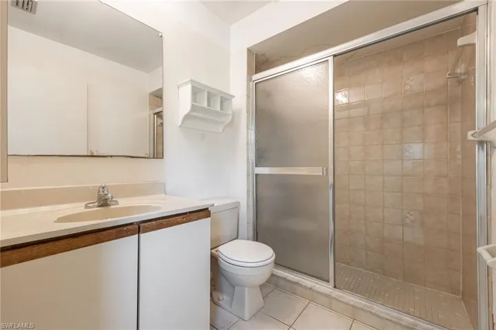 Bathroom with a sliding glass shower enclosure, beige tiled shower walls, and a white vanity with an integrated sink and light-colored countertop