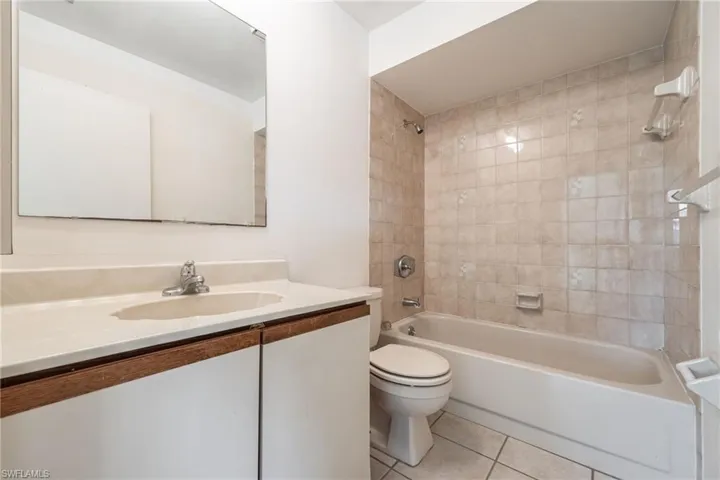 Bathroom featuring a light-toned vanity with an integrated sink, a rectangular mirror, a toilet, a bathtub, and tiled walls