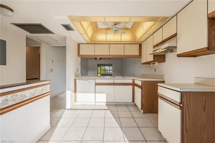 Kitchen featuring wood-finish lower cabinetry, light-toned upper cabinetry, white countertops, tile flooring, and a built-in dishwasher