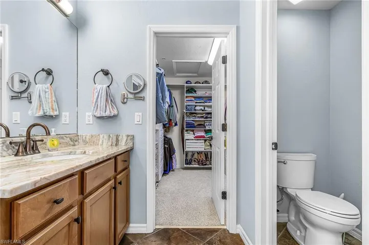 Bathroom vanity with wood cabinetry, light-toned stone countertop, and an undermount sink