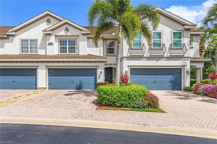Stucco exterior featuring multiple garages with blue doors, decorative iron window accents, and mature tropical landscaping