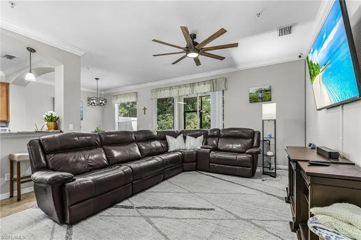 Spacious living area featuring a wood-finish ceiling fan, crown molding, and large windows with exterior views