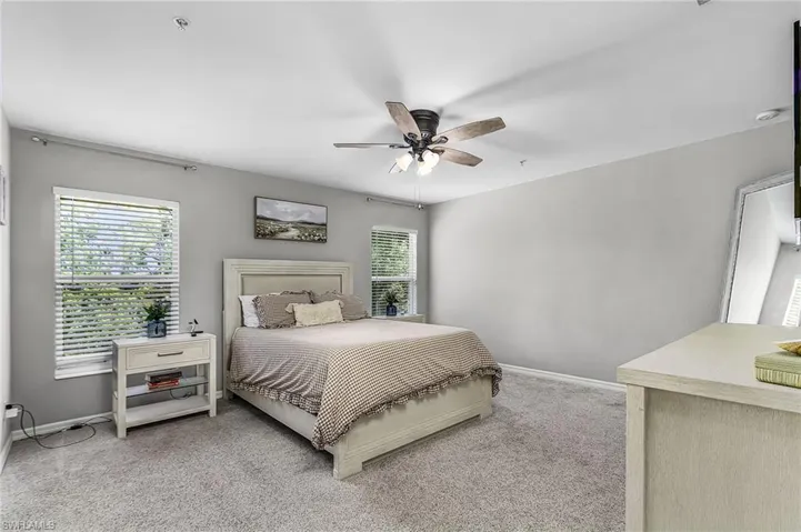 Carpeted room featuring light gray walls, two windows with blinds, and a ceiling fan with light fixture