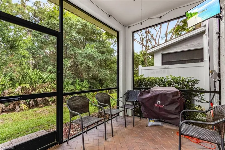 Screened patio featuring brick-finish flooring, a white privacy fence, and mature landscaping