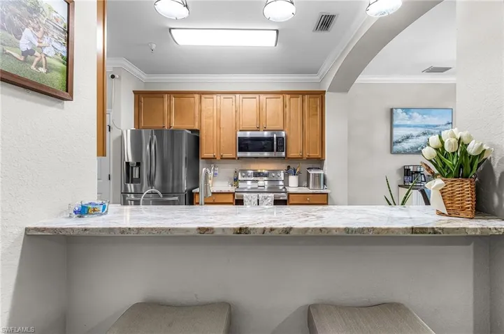 Kitchen pass-through featuring a stone countertop breakfast bar, recessed lighting, wood cabinetry, stainless steel appliances, and a tiled backsplash