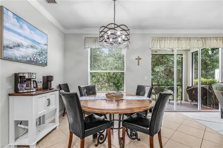 Dining area featuring a circular wood-finish table with wrought iron detailing, a contemporary chandelier, and tiled flooring