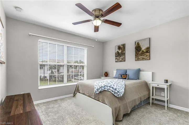 Bedroom featuring light grey walls, carpet flooring, a large window with white blinds, and a ceiling fan with wood-finish blades