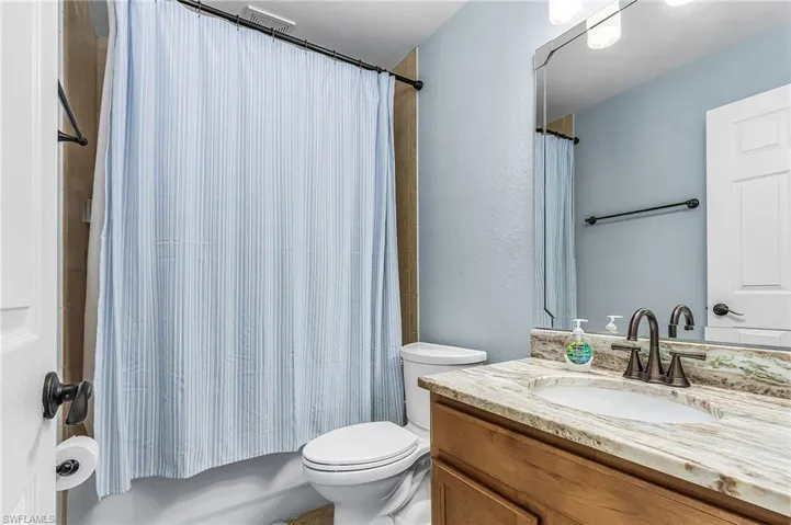 Bathroom featuring a wood-finish vanity with an oval undermount sink, a patterned countertop, and a wall-mounted mirror