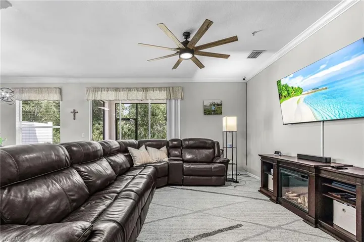 Spacious living area featuring a wood-finish ceiling fan, crown molding, large window openings, and a built-in media console with an electric fireplace