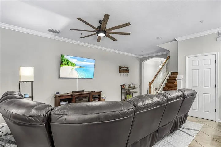 Living area featuring a multi-blade ceiling fan with integrated lighting, crown molding, and light-toned wall paint