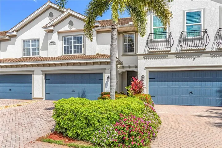 Mediterranean-style townhome with white stucco exterior, terracotta roof tiles, and blue garage doors