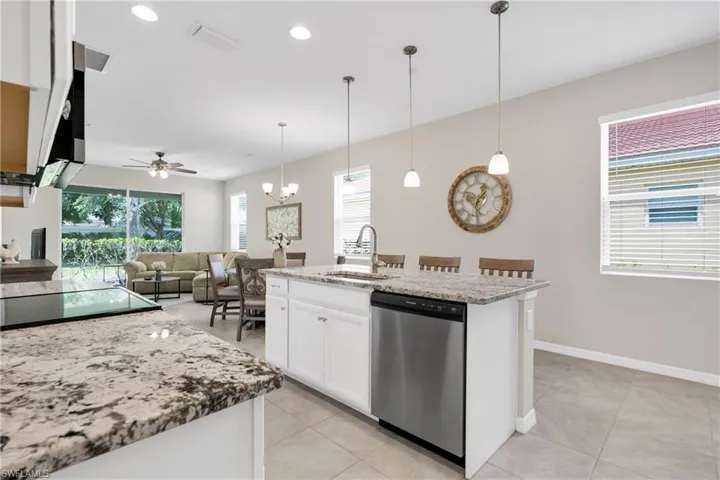 Kitchen featuring light stone counters, a sink, white cabinetry, dishwasher, and decorative light fixtures