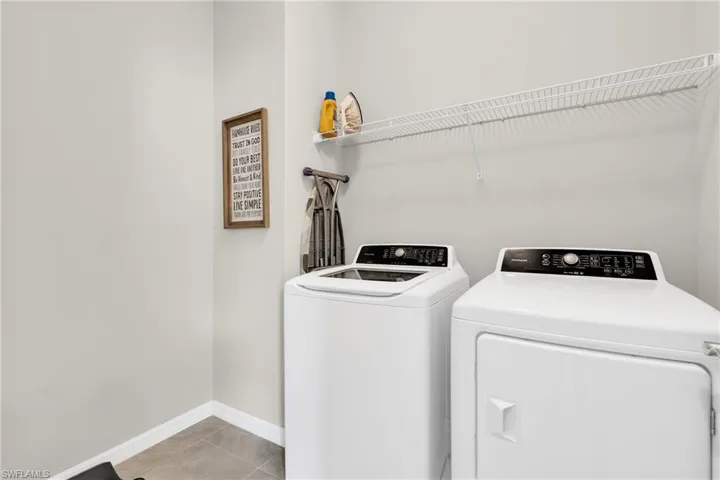 Washroom featuring light tile patterned floors, washer and clothes dryer, baseboards, and laundry area