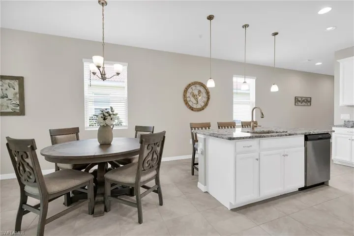 Kitchen featuring light stone countertops, an island with sink, a sink, stainless steel dishwasher, and a notable chandelier