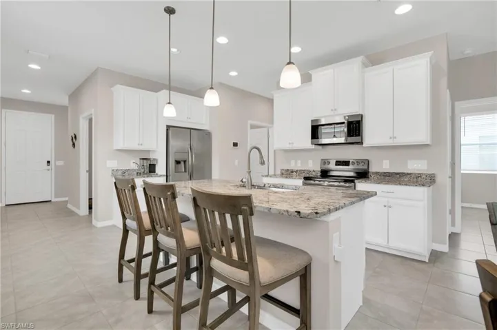 Kitchen featuring recessed lighting, a center island with sink, appliances with stainless steel finishes, a sink, and a breakfast bar area