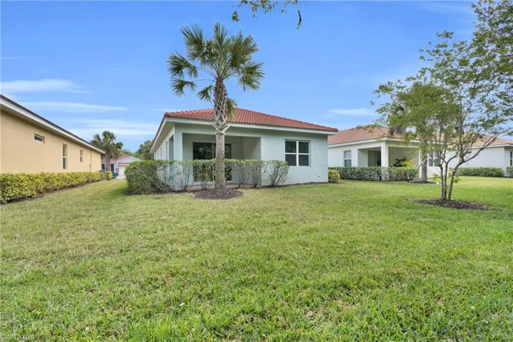 Back of house with a lawn, a tiled roof, and stucco siding