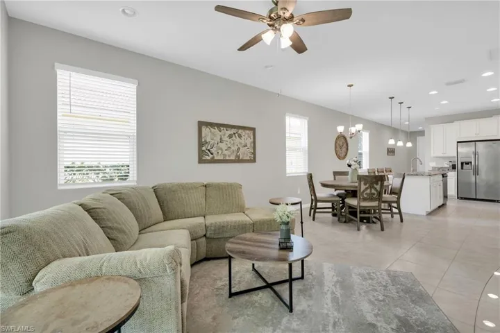 Living area with light tile patterned floors, ceiling fan with notable chandelier, and recessed lighting