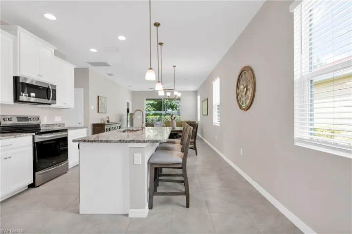 Kitchen with white cabinets, light stone countertops, appliances with stainless steel finishes, an island with sink, and a sink