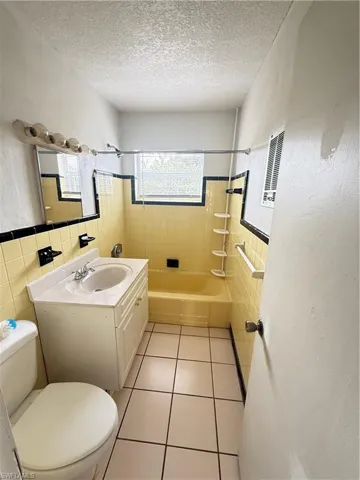 Full bath with vanity, tile walls, light tile patterned floors, a wainscoted wall, and  shower combination