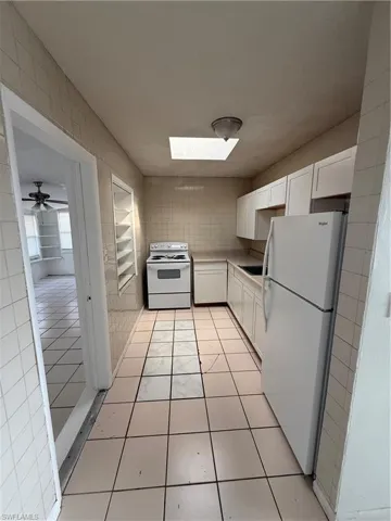 Kitchen with refrigerator, tile walls, white cabinetry, stove, and light countertops