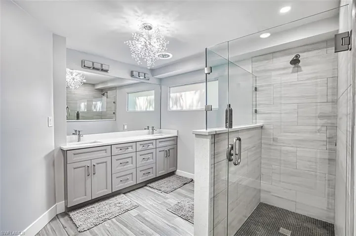 Bathroom with a stall shower, double vanity, light wood-style floors, and a chandelier