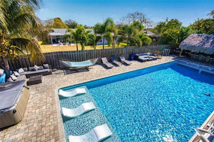 View of swimming pool featuring an outdoor living space with a fire pit, patio surround, a fenced backyard, and a hot tub