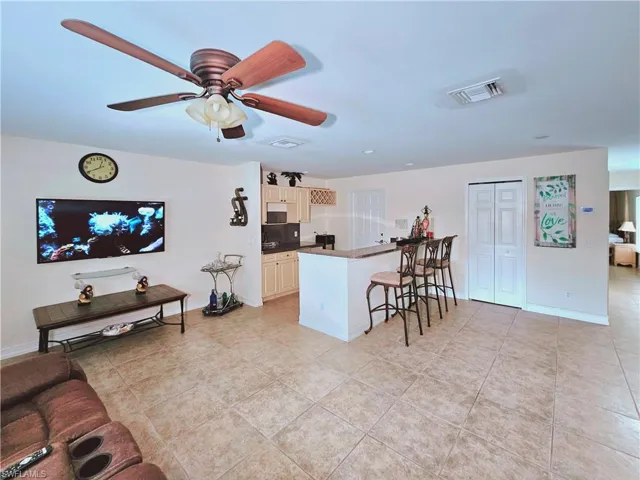 Kitchen featuring a kitchen breakfast bar, light tile patterned floors, ceiling fan, a peninsula, and dark countertops