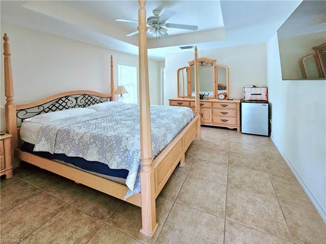 Bedroom with a tray ceiling, refrigerator, light tile patterned floors, and a ceiling fan
