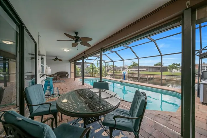 Swimming pool with glass enclosure, a sunroom, a ceiling fan, a water view, and a patio area