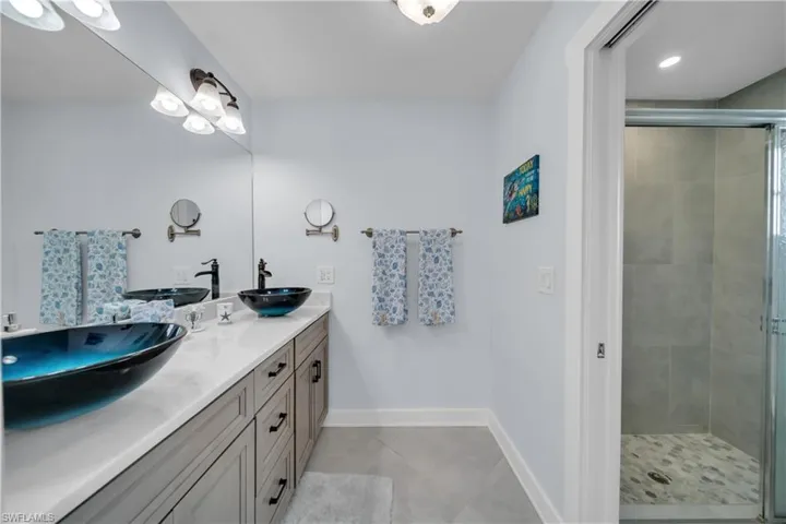 Bathroom featuring a shower stall, double vanity, and light tile patterned flooring