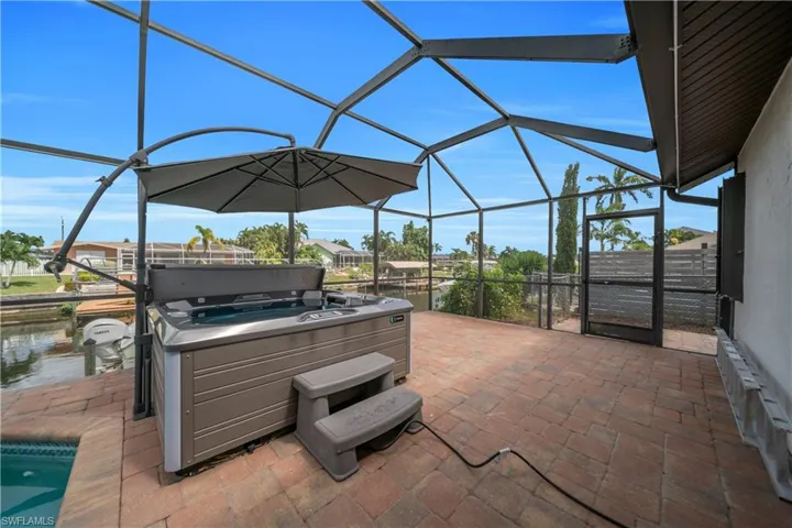 View of patio with a lanai, a sunroom, a hot tub, an outdoor pool, and a water view