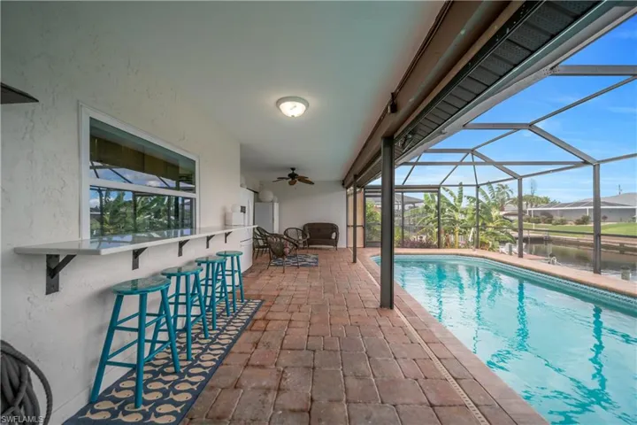 Outdoor pool featuring a sunroom, a lanai, a water view, a patio area, and a ceiling fan