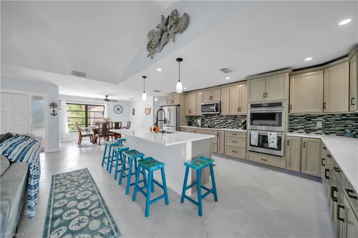 Kitchen with open floor plan, a h kitchen island with sink, a kitchen bar, pendant lighting, and stainless steel appliances