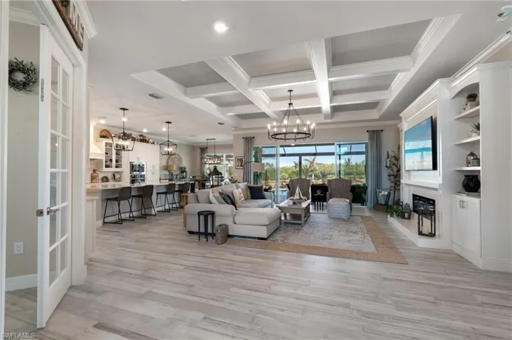 Living room with coffered ceiling, beam ceiling, crown molding, and a chandelier