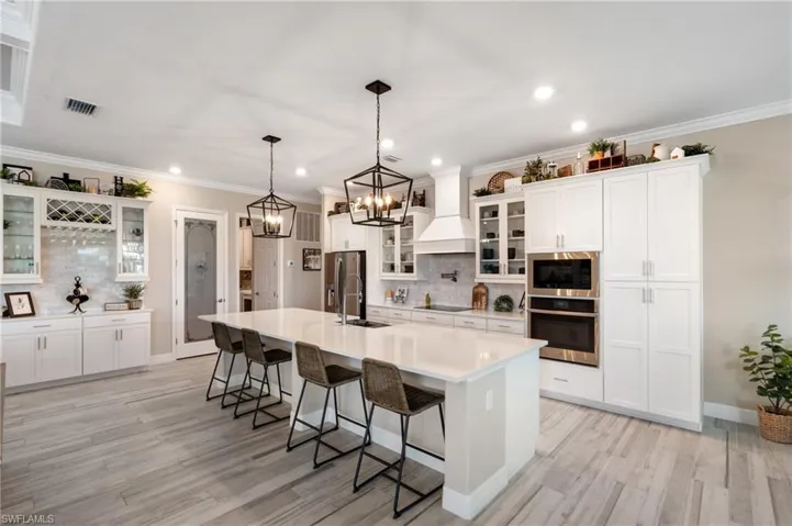 Kitchen featuring a kitchen breakfast bar, hanging light fixtures, stainless steel appliances, custom range hood, and a center island with sink