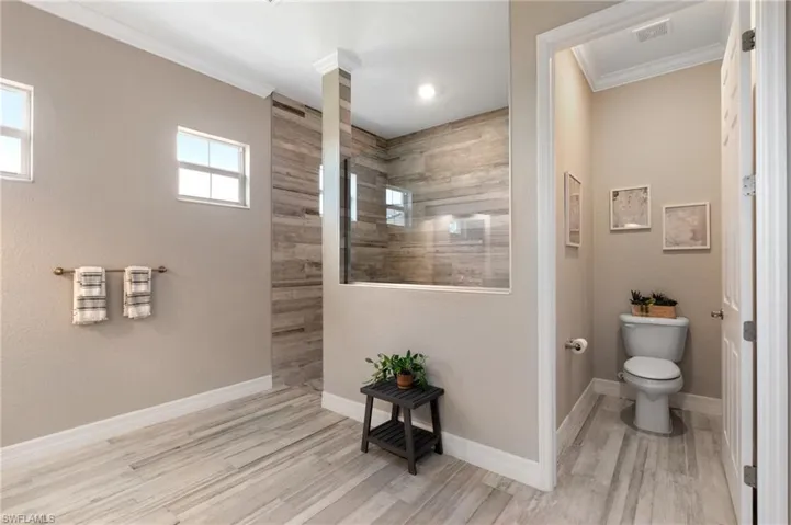 Primary bathroom featuring ornamental molding, wood-type flooring, tiled shower, and toilet