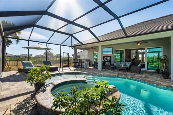 View of pool featuring ceiling fan, a patio, glass enclosure, an outdoor hangout area, and exterior bar