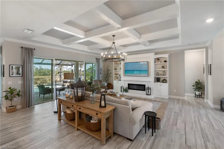 Living room featuring crown molding, light hardwood / wood-style flooring, an inviting chandelier, beam ceiling, and coffered ceiling