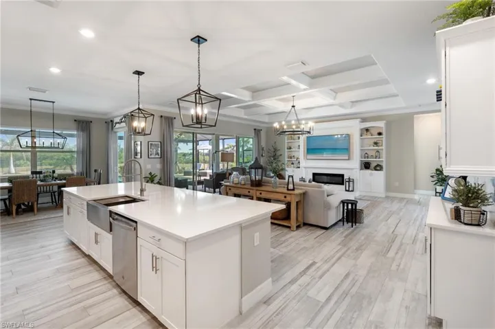 Kitchen featuring pendant lighting, white cabinetry, dishwasher, sink, and a center island with sink