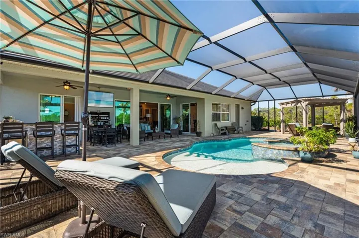 View of pool featuring a patio area, glass enclosure, an outdoor bar, an in ground hot tub, and ceiling fan