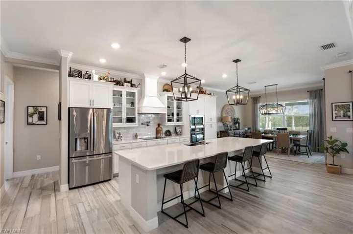 Kitchen with a large island, a breakfast bar, premium range hood, white cabinetry, and appliances with stainless steel finishes